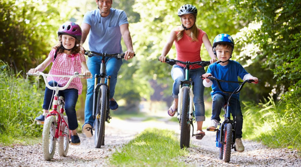 Mutter, Vater und zwei Kinder fahren Fahrrad auf einem Waldweg