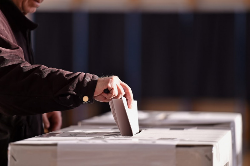Jemand steckt einen Stimmzettel in eine Wahlurne
